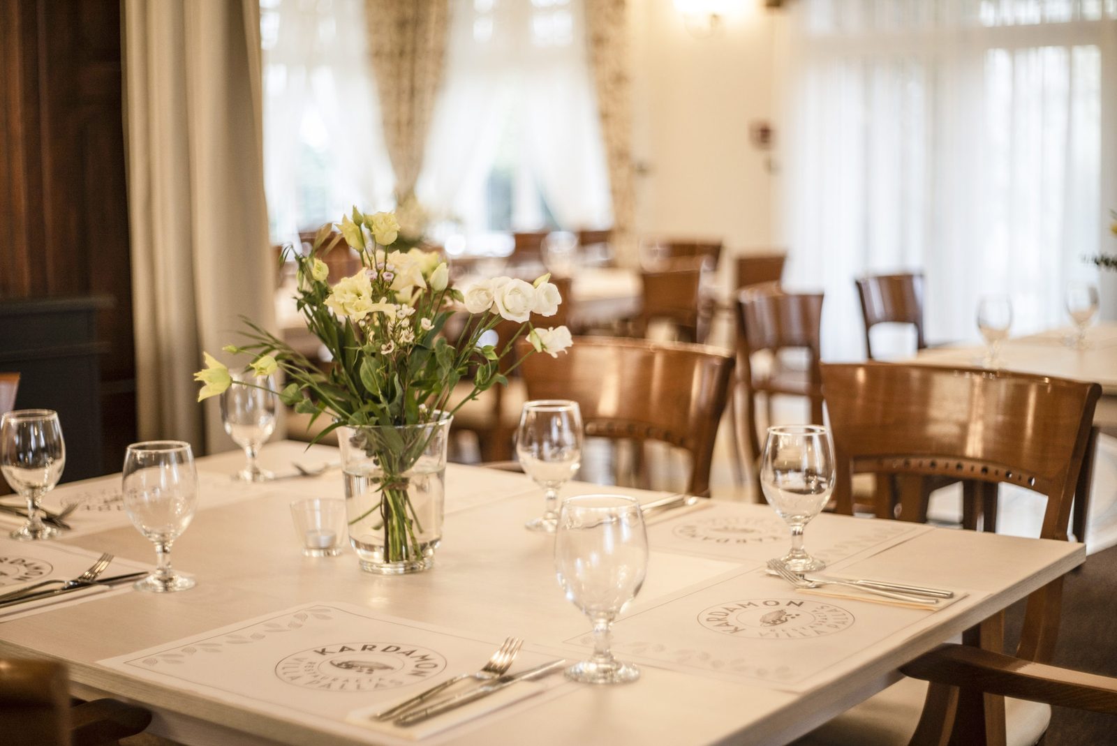 Salon restauracji Kardamon — nakryty stół z logo i kwiatami